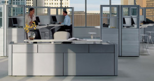 A man and a woman sitting in grey color refurbished cubicles.